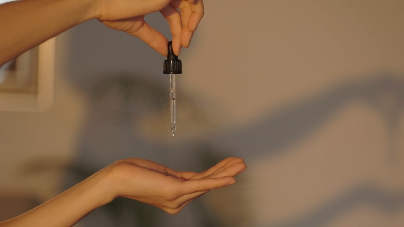 A Hand Holding a Dropper Bottle Dispensing Rosemary Oil Into the Palm